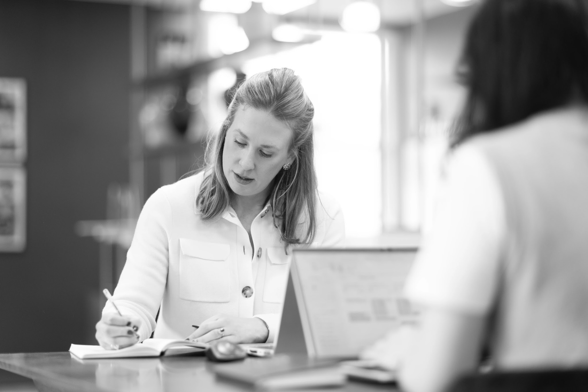 Recruitment consultant noting details of a temp brief in a notebook during a meeting