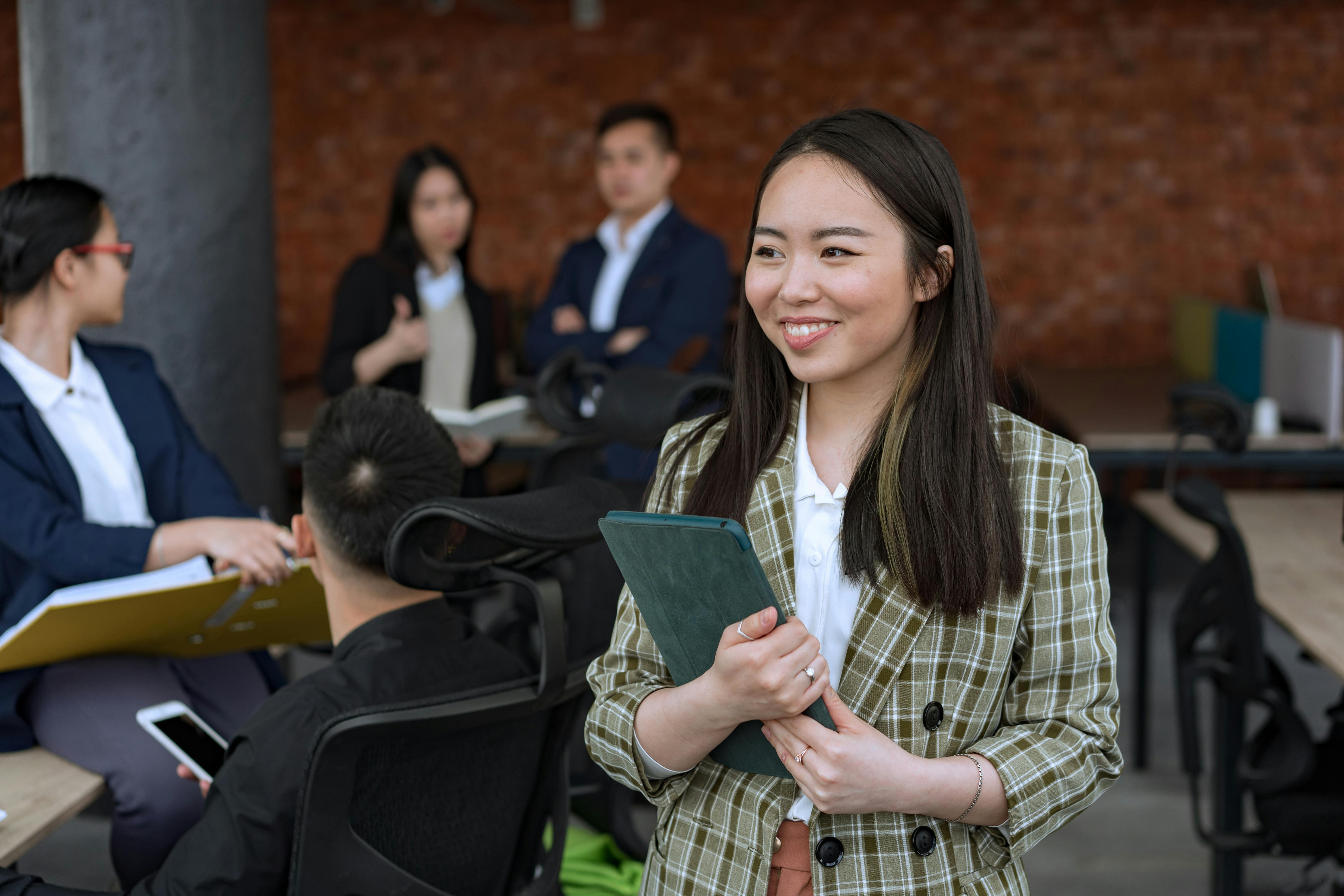 A personal assistant in a green plaid blazer smiling and holding files to her chest.