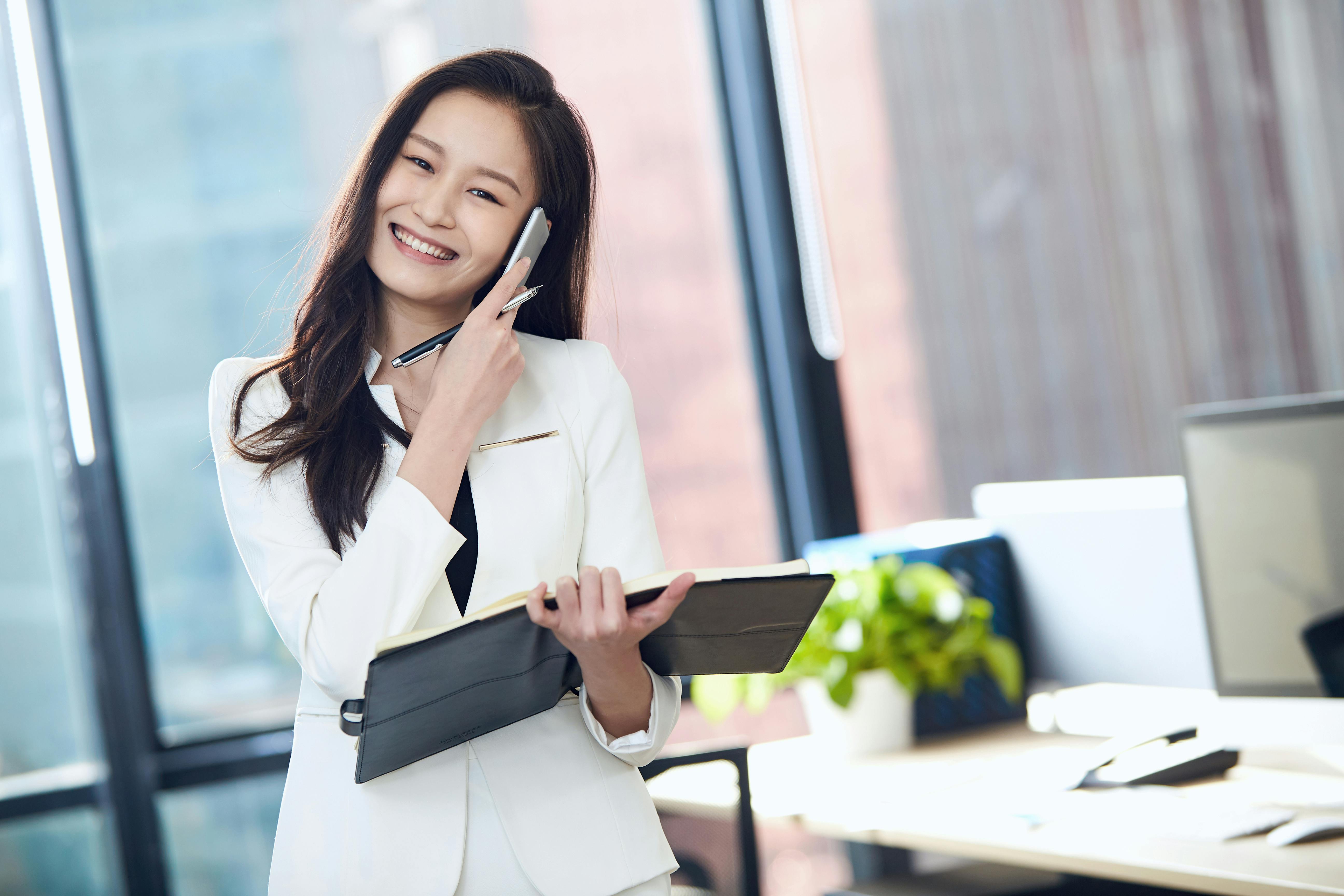 A PA is speaking to her executive on her phone while carrying a folder.