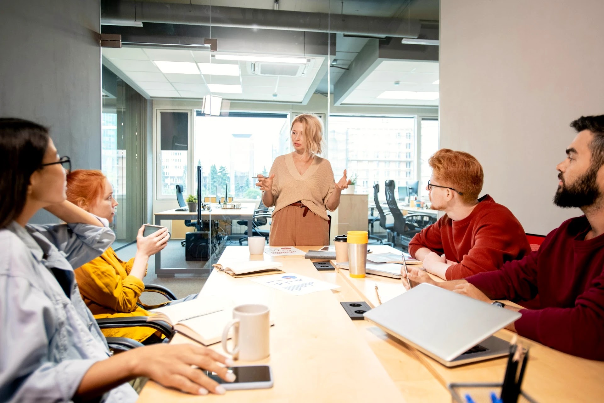 Management consultant leading a team discussion around a meeting table by a window