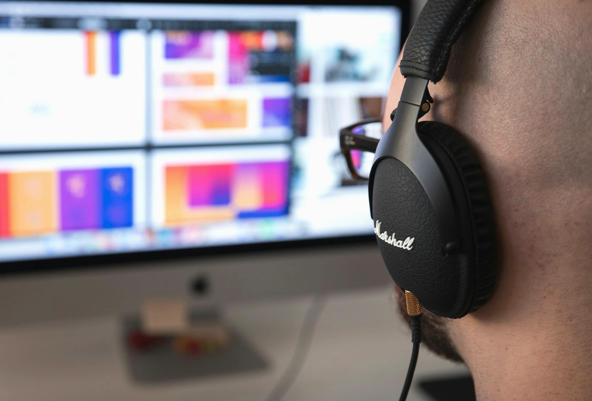 Creative professional wearing headphones at a desktop screen showing colourful design work