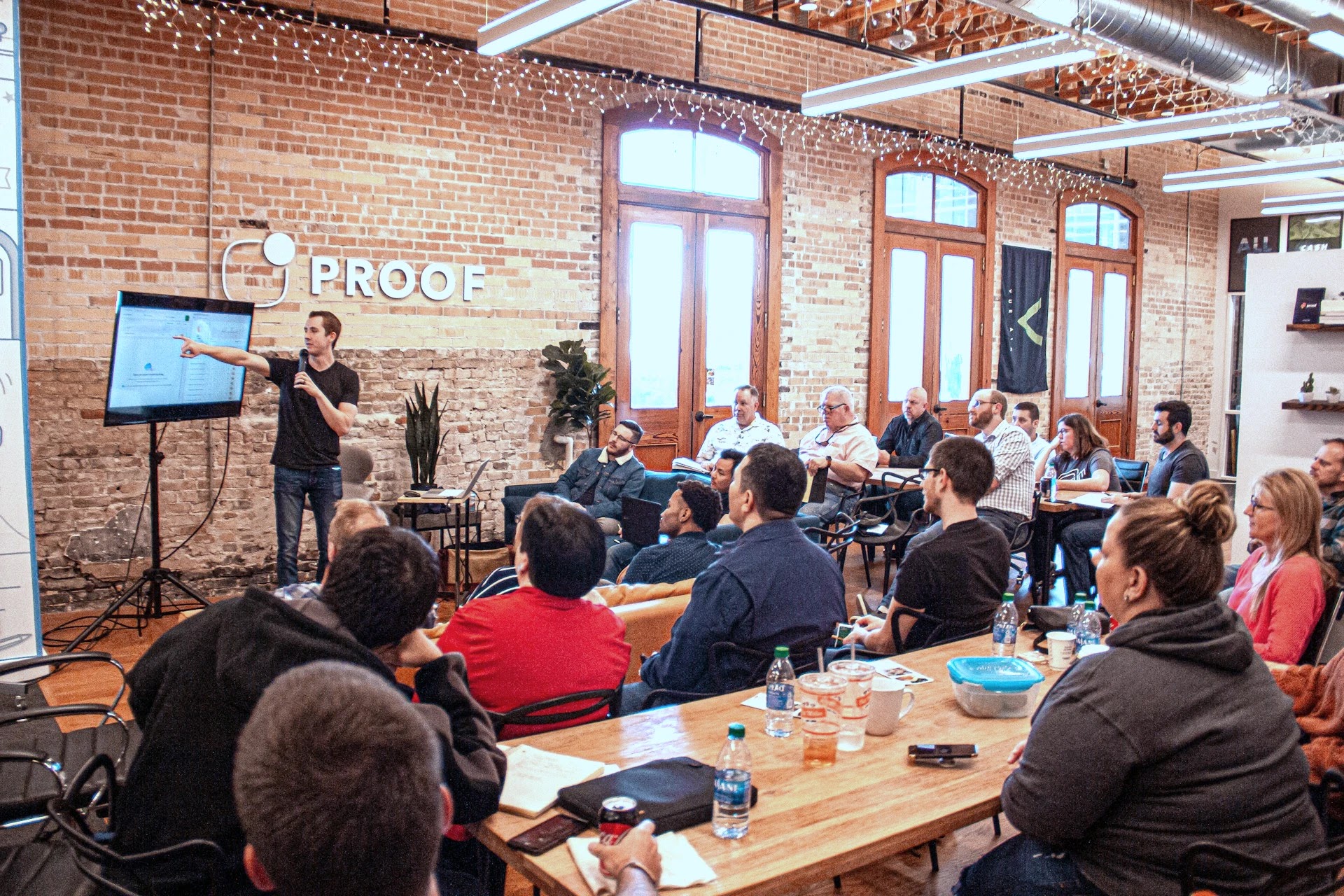 Founder presenting to a seated audience at a start-up meet-up in a brick-walled workspace