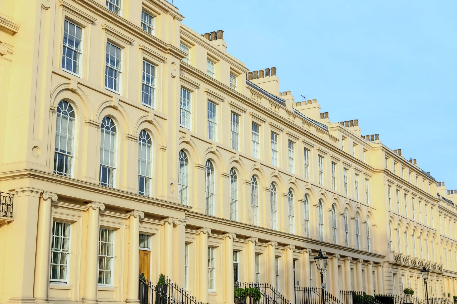 Row of grand cream-stucco Regency townhouses on a London terrace under a blue sky