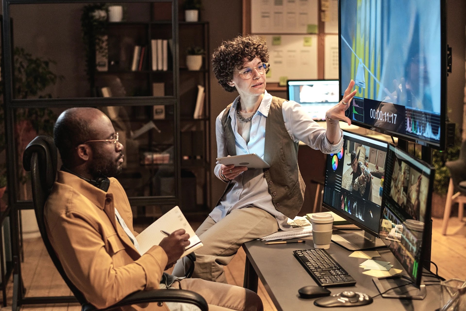 Two media professionals reviewing video footage on multiple editing screens in a studio