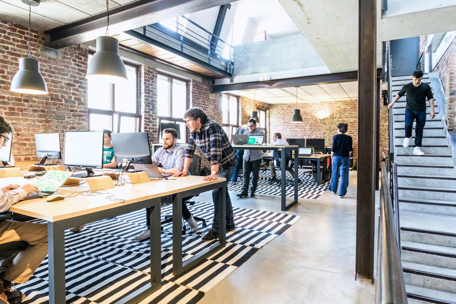 Open-plan start-up office with exposed brick, shared desks and staff working across two levels