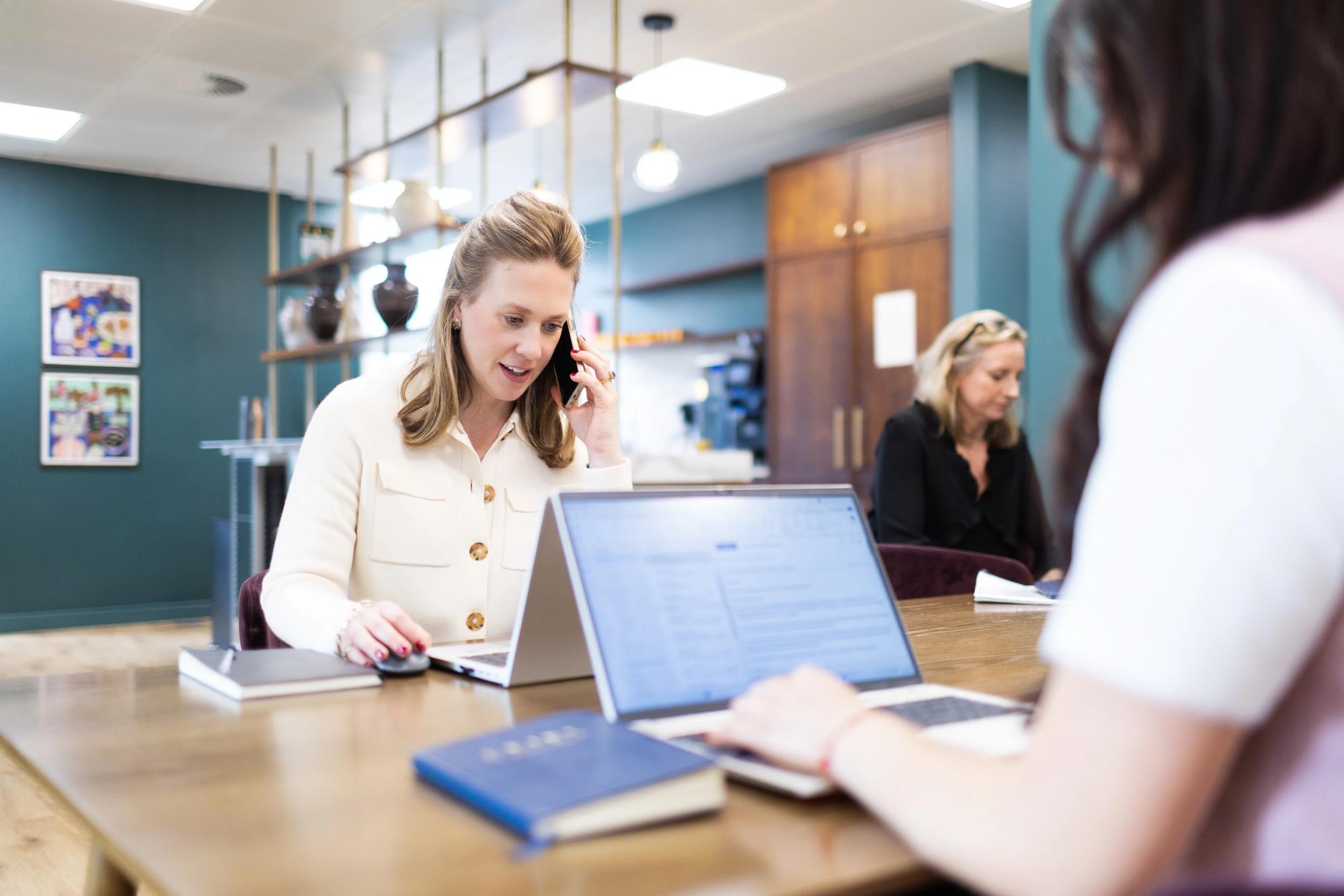 Private office recruitment specialist on the phone at a laptop while a colleague works nearby in a discreet office
