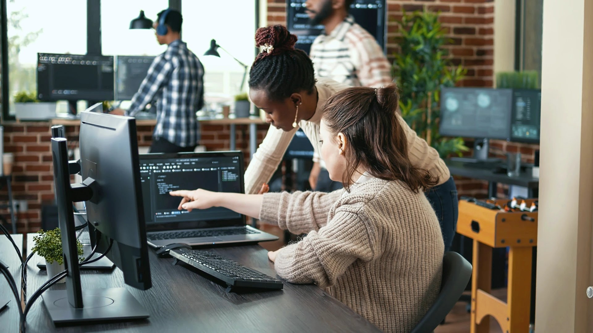 Software developers reviewing code together at a multi-screen workstation in a tech office
