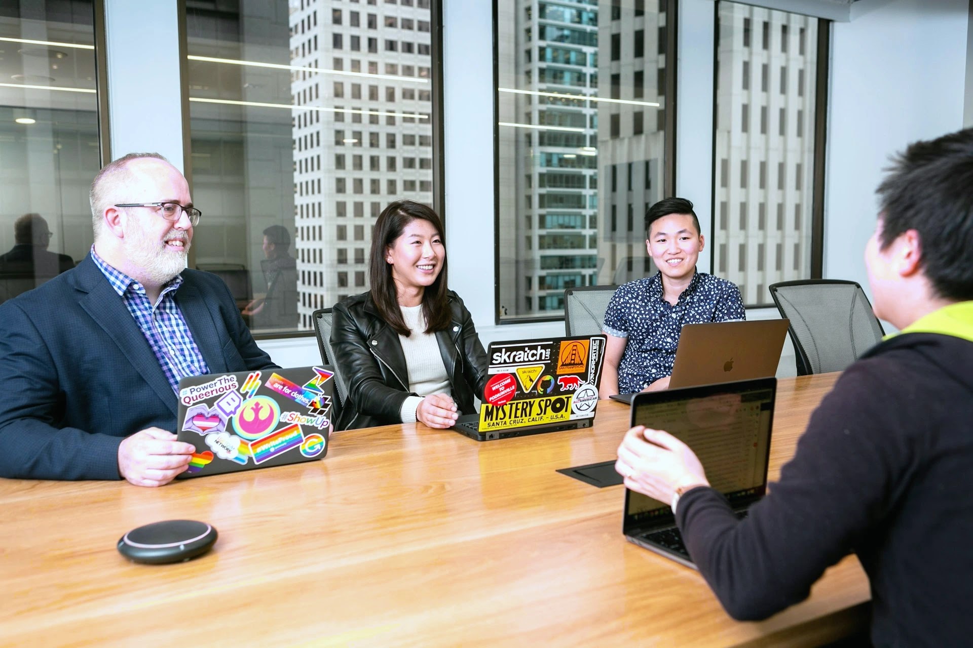 Tech team in a relaxed meeting around laptops in a high-rise office with city views