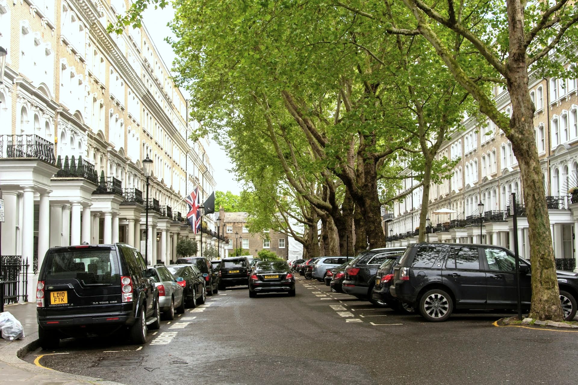Tree-lined Kensington street of white stucco townhouses with parked cars